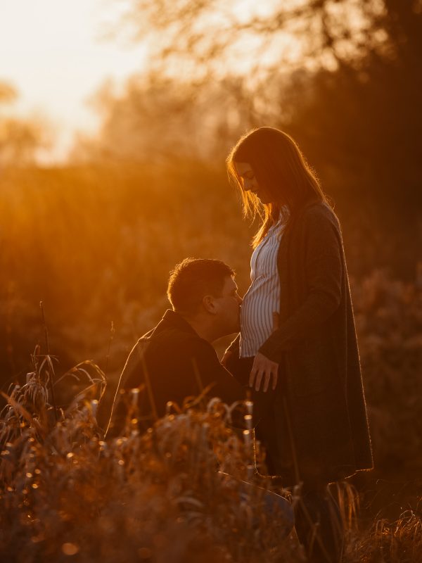 Babybauchshooting. Junges Paar im Sonnenuntergang. Mann küsst ihren Bauch.